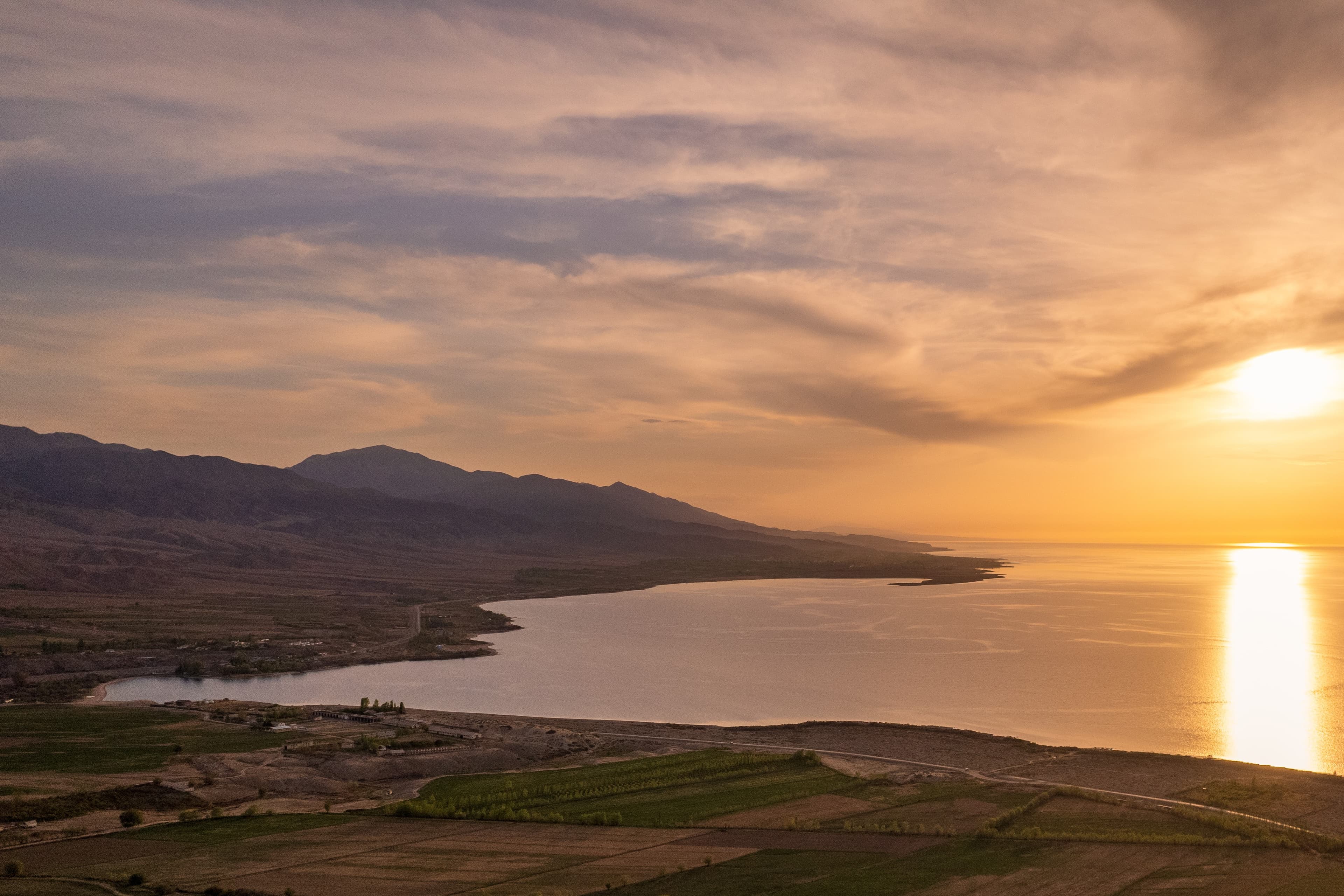 View by drone of the shore of Issyk Kul lake between Tamga and Tosor villages, on the right side sunset on the lake Issyk Kul, on the left side feet of the Teskei Alatoo range